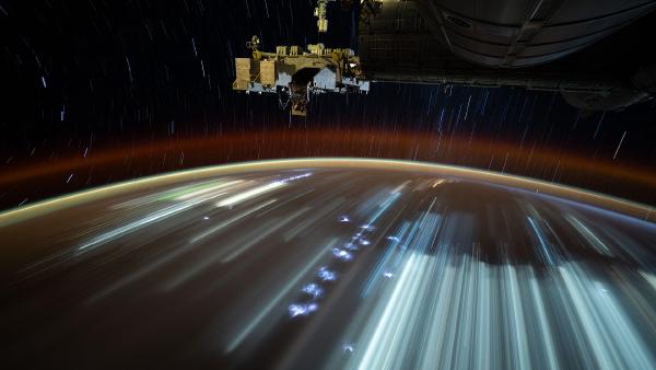 City lights streak below, taken from the International Space Station (© NASA)